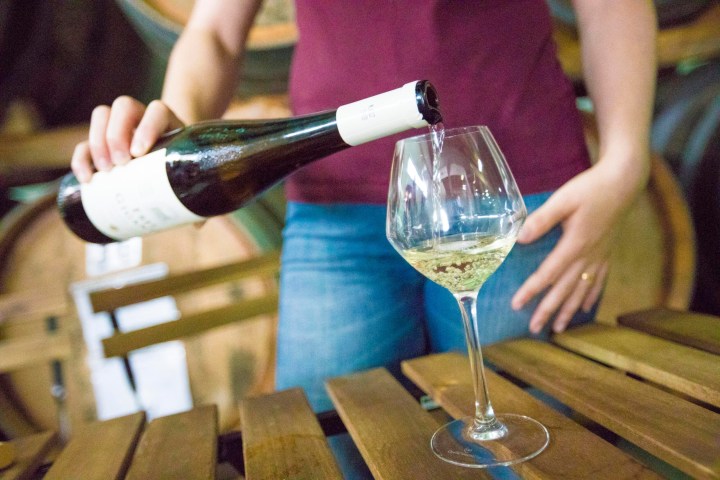 Person pouring white wine into a glass in a wine cellar.