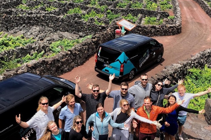 Group of people waving near two vans on a road through a green, rocky landscape.