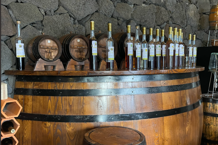 Wooden barrels and bottles on a bar with a stone wall backdrop.