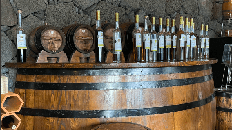 Wooden barrels and bottles on a bar with a stone wall backdrop.