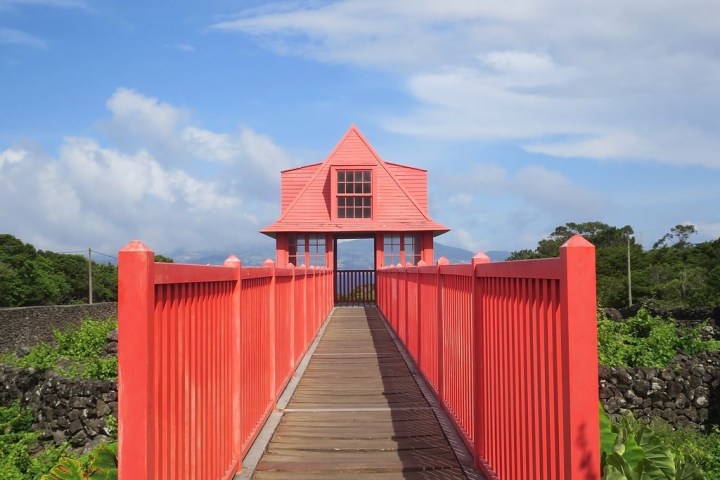 Red bridge leading to a small, pink building under a blue sky.