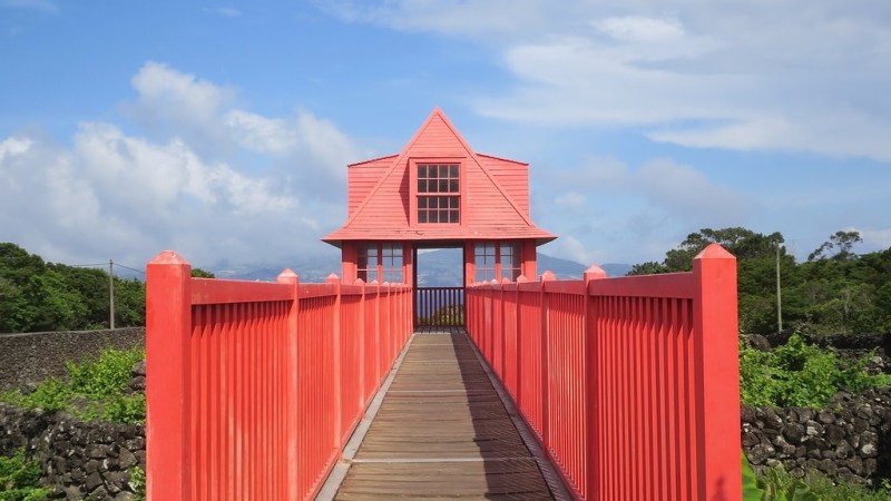 Red bridge leading to a small, pink building under a blue sky.