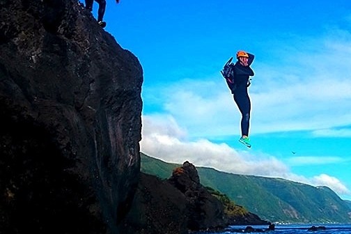 Two people cliff jumping into the ocean on a sunny day.