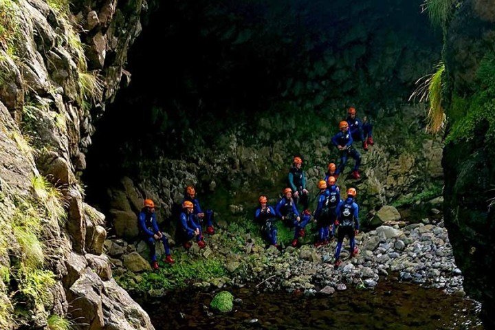 Group of people in helmets exploring rocky cave with greenery.