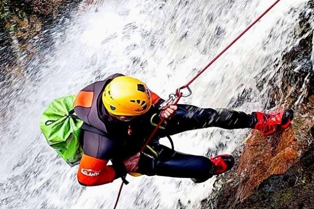Person canyoneering down a waterfall with helmet, rope, and climbing gear.