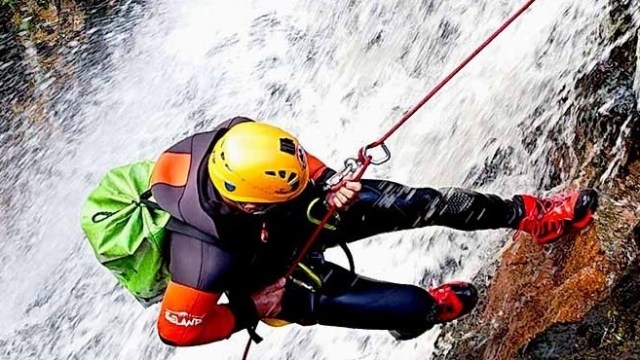 Person canyoneering down a waterfall with helmet, rope, and climbing gear.