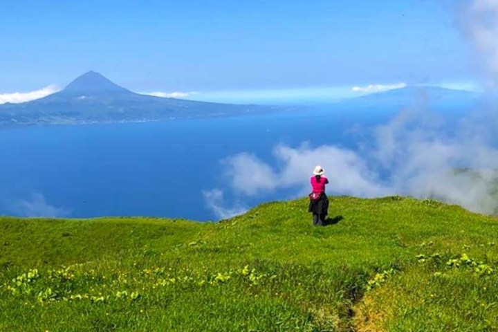 Person on grassy hill overlooking ocean and distant mountain on a clear day.
