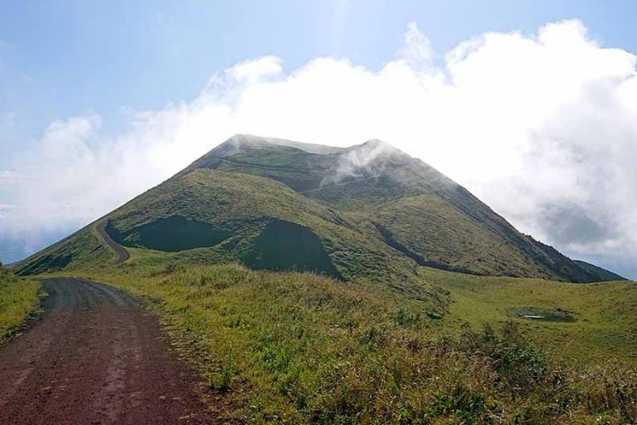 Dirt road leading to a grassy hilltop under a partly cloudy sky.