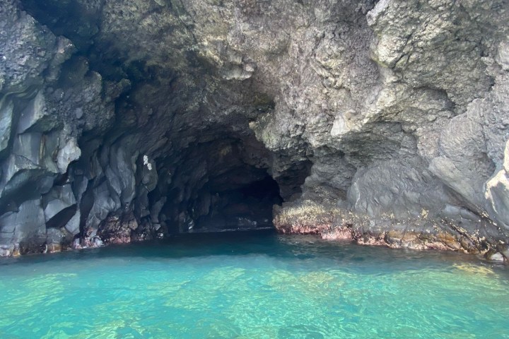 Rocky cave entrance with clear turquoise water.
