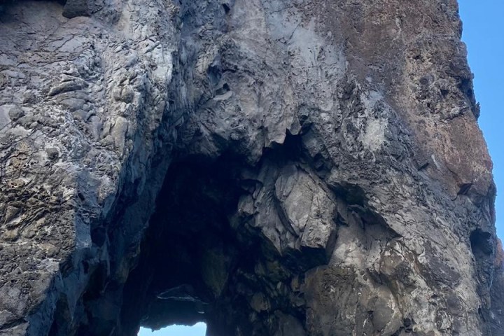 Person in a boat approaching a large rock arch formation with blue sky.