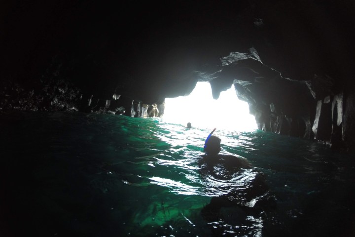 People snorkeling inside a dark cave with light at the exit.