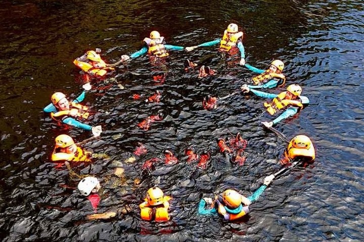 Group of people in life jackets hold hands forming a circle in water.