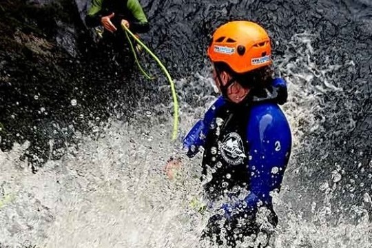 Two people canyoning; one wearing an orange helmet, rappelling through a waterfall.