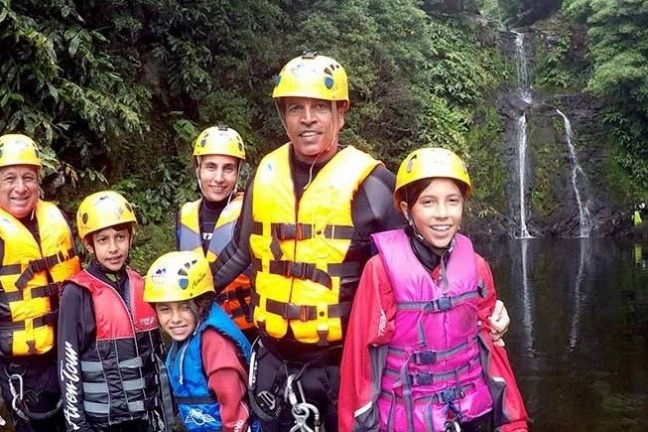 Group of people in life vests and helmets near a waterfall in a forest setting.
