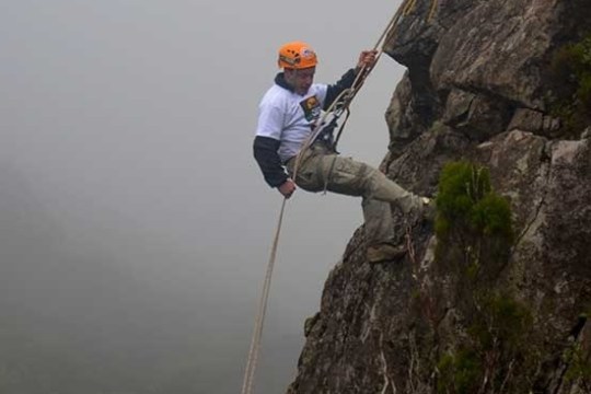 Person rock climbing on a steep cliff with safety gear, surrounded by mist.
