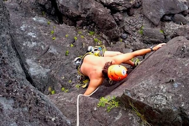 Person rock climbing a steep, rocky surface with a helmet and safety gear.