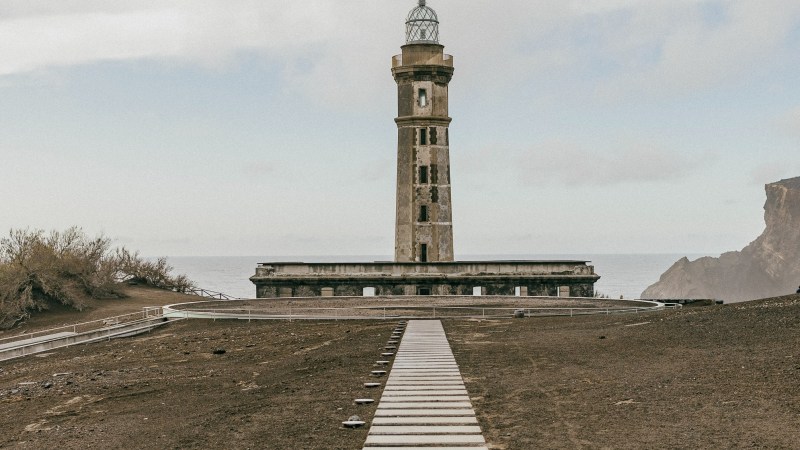 Stone path leading to a tall lighthouse with a cloudy sky background.