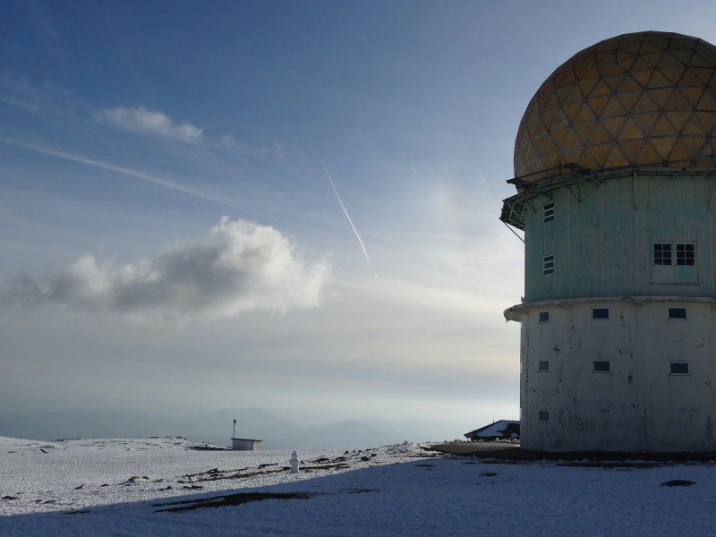 Large geodesic dome on snowy mountaintop under clear sky.