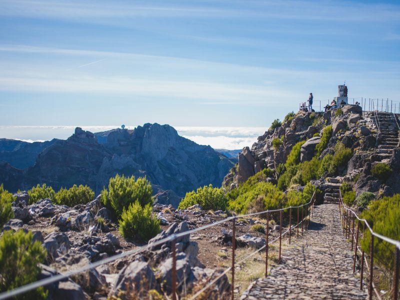 Mountain pathway with railing leading to a viewpoint, distant peaks visible.