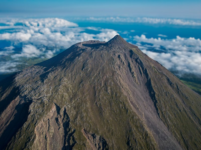 Aerial view of a volcanic peak with surrounding clouds.