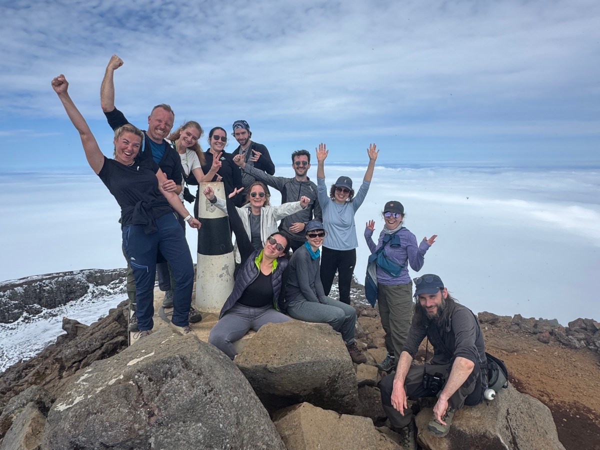 Group of hikers celebrating on a rocky mountaintop with clouds below.